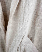 Nahaufnahme eines beigen, strukturierten Stoffes mit sichtbaren Nähten und Falten, wahrscheinlich Teil des übergroßen Kimonos Solana von Main Design.