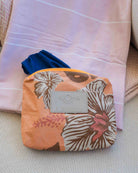 Ein blauer Badeanzug lugt teilweise aus einer „Aloha Collection Aloha Small Pouch“ in pfirsichfarbenem Blumenmuster mit der Aufschrift „ALOHA“ hervor – einer stilvollen Bikini-Tasche, die auch als wasserdichte Tasche dient und auf gefalteten rosa Handtüchern mit gemusterter Oberfläche darunter liegt.