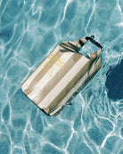 Ein gestreifter, wasserdichter Dry Bag von Meraki Supply Co. by Main Design schwimmt auf klarem, blauem Poolwasser und erzeugt sanfte Wellen - ideal für Ihr nächstes Outdoor-Abenteuer.