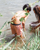 Zwei Kinder in Main Design Lean Boardshorts für Jungen stehen im flachen Wasser und erforschen zwischen grünen Pflanzen - eines mit einem Netz, das andere mit einem Eimer.