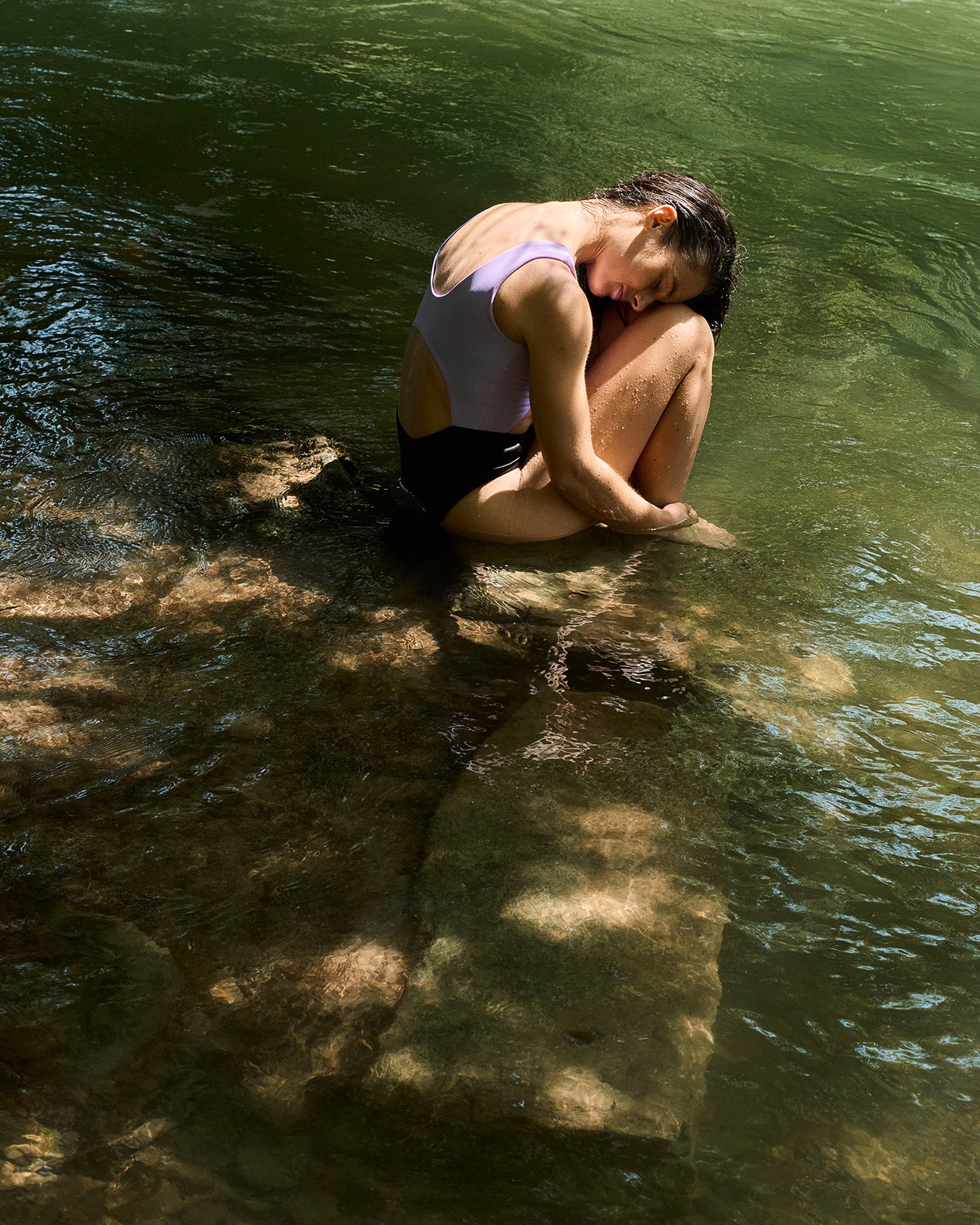 Frau sitzt auf Stein im Fluss in einem Badeanzug von MAIN Design in violett