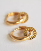 Ein Paar Ohrringe Kreolen von Adorabili, handgefertigt in Frankreich, mit flachen runden Anhängern und gravierten Linien, präsentiert vor weißem Hintergrund.