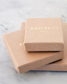 Drei hellbraune Pappschachteln, zwei gestapelt und eine angelehnt, tragen das goldene "Adorabili"-Logo - die perfekte Verpackung für den Adorabili-Ring, der in Frankreich für Kinder handgefertigt wird.