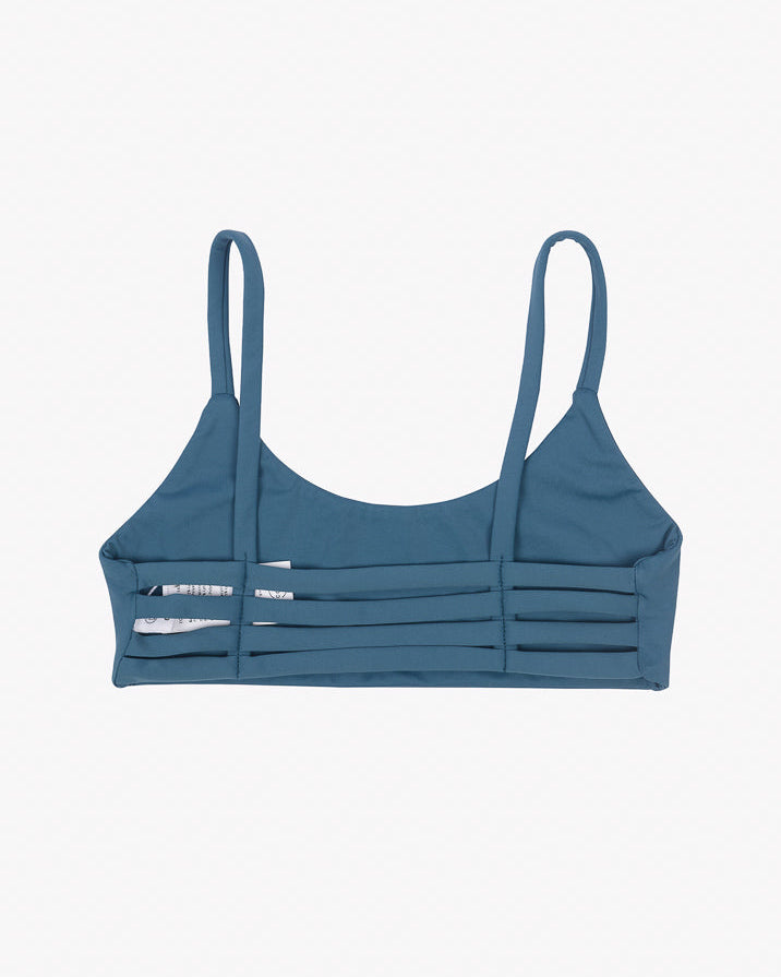 Das Sassy Bikini-Top von Main Design ist ein blaugrünes Bikini-Oberteil mit minimalistischem Design aus recycelten Materialien. Es verfügt über dünne Schulterträger und horizontale Aussparungen, ergänzt durch einen nahtlosen Schnitt für modernes Flair, alles vor einem schlichten weißen Hintergrund.