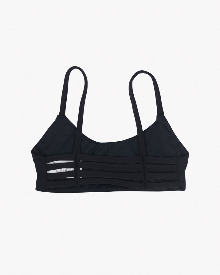 Das Sassy Bikini-Top von Main Design ist ein eleganter schwarzer Stil mit dünnen Trägern, einem Mesh-Panel-Design und einem nahtlosen Schnitt. Es hat horizontale Streifen und ein kleines weißes Logo auf der linken Seite, das aus recycelten Materialien gefertigt ist und sich elegant auf einem schlichten weißen Hintergrund abhebt.