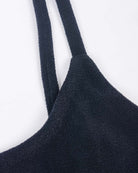 Nahaufnahme des Sassy Bikini-Tops von Main Design aus strukturiertem schwarzem Recyclingstoff mit dünnen Trägern vor weißem Hintergrund. Die raue, taktile Oberfläche des Kleidungsstücks verkörpert mühelos den Stil eines Sassy Bikini-Tops.