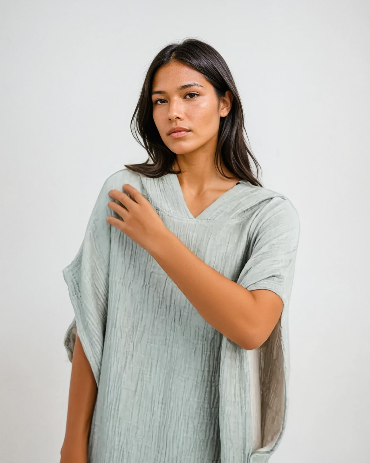 Eine Frau mit langen dunklen Haaren trägt den Shoreline Breeze Poncho von Main Design in One Size, steht vor einem schlichten weißen Hintergrund und blickt selbstbewusst mit erhobenem Arm in die Kamera.
