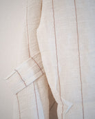 Nahaufnahme des Soleil Kimono von Main Design, der cremefarbene, strukturierte Stoff aus 100% Baumwolle mit dünnen vertikalen braunen Streifen und einem detaillierten Ärmel oder Träger.