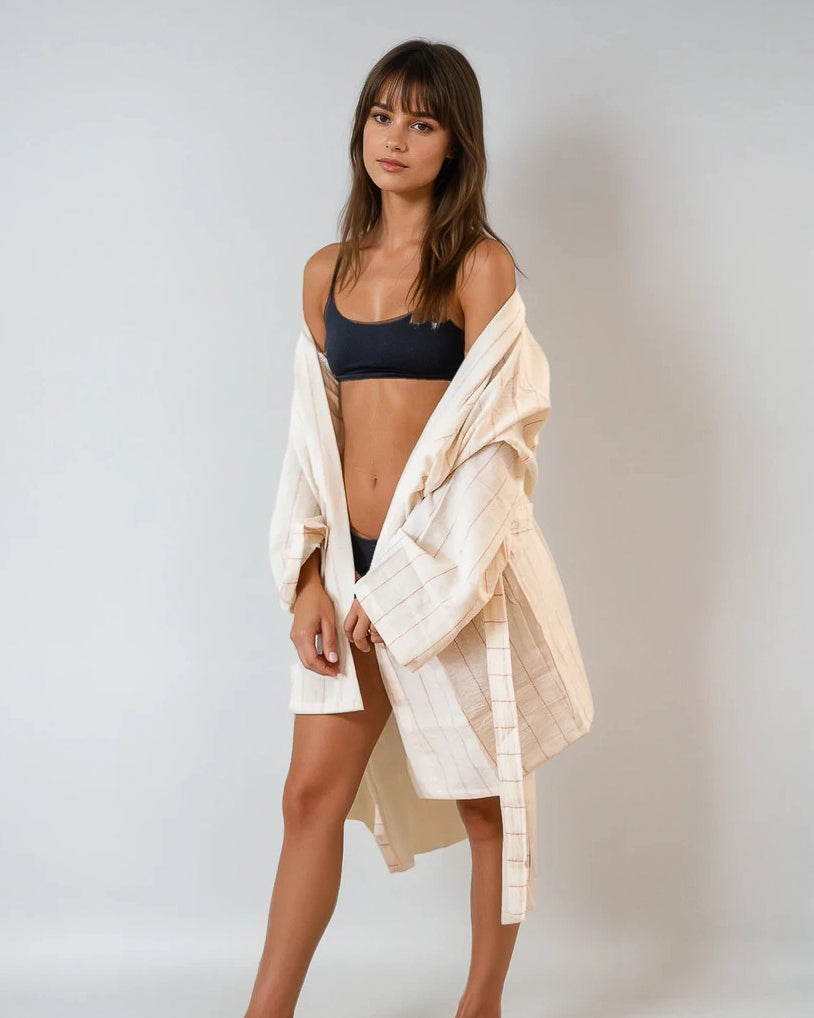 Eine Frau mit glattem braunem Haar und Pony steht vor einem schlichten, hellen Hintergrund, trägt einen schwarzen BH und Unterwäsche und hat den Kimono von Main Design Soleil - hergestellt aus 100% Baumwolle in nachhaltiger Produktion - über die Schultern gehängt.