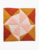 Die Spielmatte und Krabbeldecke Boot von Main Design ist eine quadratische, handgefertigte Steppdecke mit einem geometrischen Muster aus Dreiecken und Vierecken in warmen Rot-, Orange-, Gelb- und Rosatönen. Das Design bildet in der Mitte ein kreisförmiges Motiv auf weißem Hintergrund und eignet sich daher ideal als Spielmatte oder Krabbeldecke für die Kleinen.