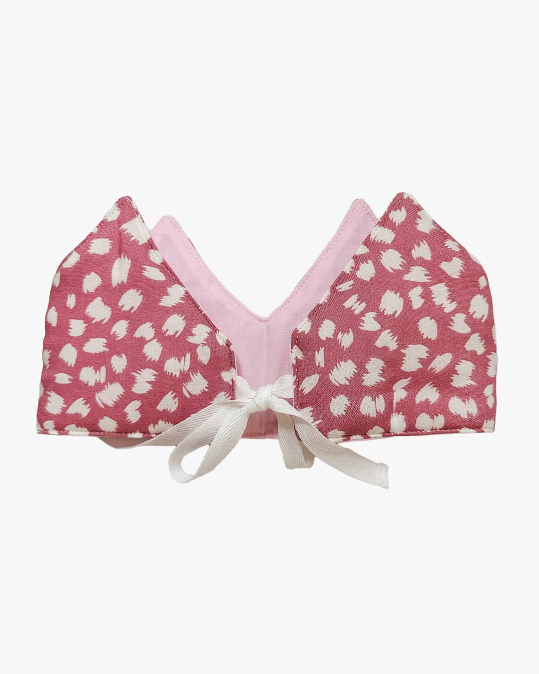 Die Stoffkrone von Several Needs reversibel von Main Design ist eine handgefertigte, rosa und weiß gemusterte Stoffkrone aus Bali, die mit hellrosa Stoff gefüttert und vorne mit einer weißen Schleife gebunden ist.