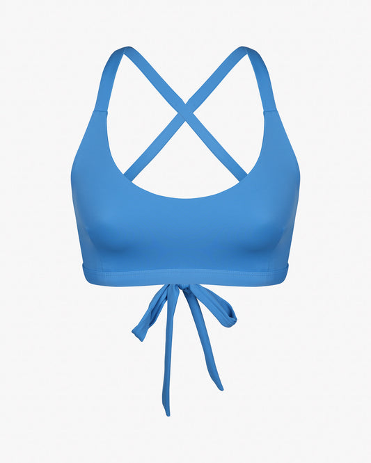 Das Charm Surf Bikini Oberteil von Main Design ist ein blaues Oberteil mit überkreuztem Rücken und Bindeverschluss vorne, gefertigt aus chlorbeständigem Stoff für Wassersport, präsentiert auf einem schlichten weißen Hintergrund.