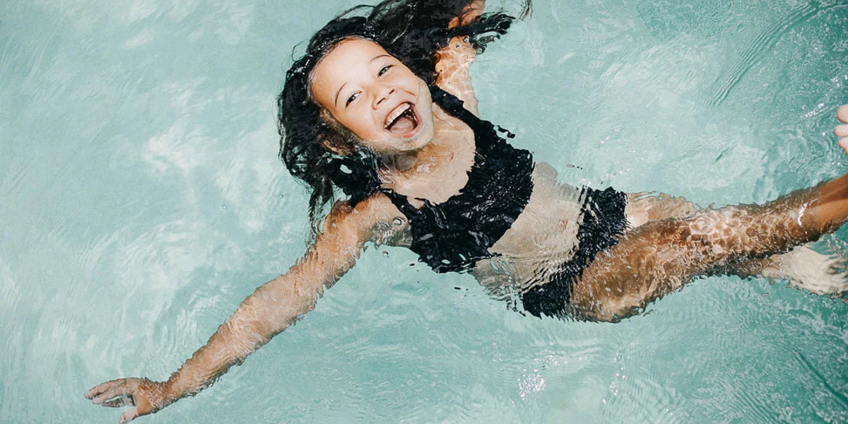 Mädchen in nachhaltigem Bikini schwimmt im Pool und lacht in die Kamera