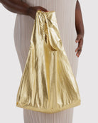 BAGGU Standard Tragetasche in Gold Metallic: Goldfarbene Metallic-Tragetasche an der Hand getragen.