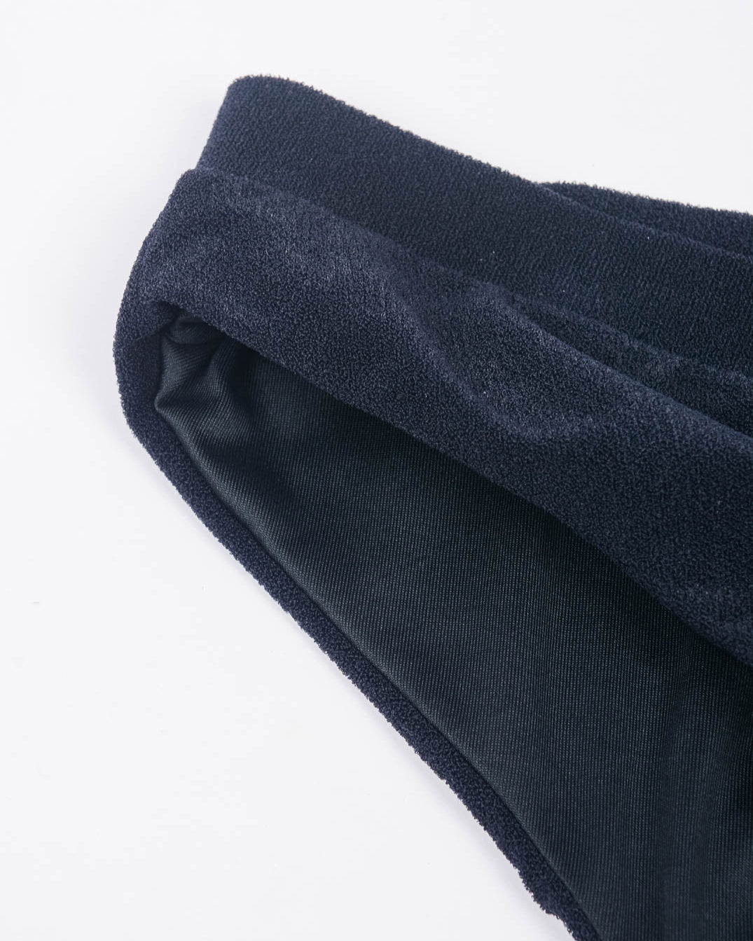 Eine Nahaufnahme des Bunds und des Stoffes der Ember Bikinihose von Main Design. Die schwarze Unterwäsche hat eine weiche, leicht gerippte Textur mit einem umgeschlagenen Bund. Hergestellt aus recycelten Materialien vor einem schlichten weißen Hintergrund.